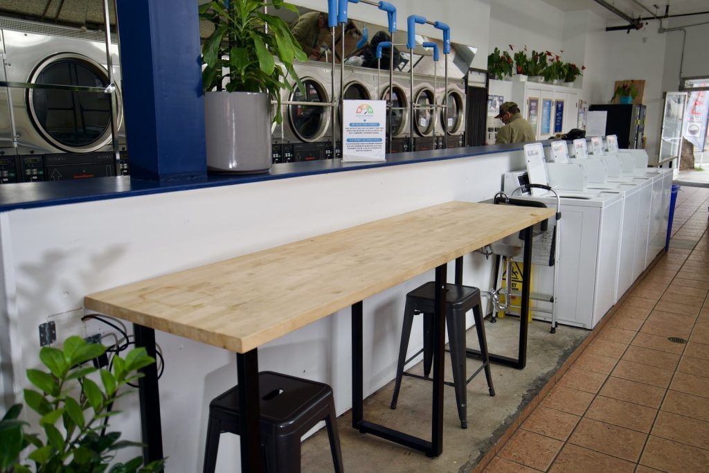 Butcher block folding counter with stools and plants beside the machine aisle at The Laundry Hub in San Francisco