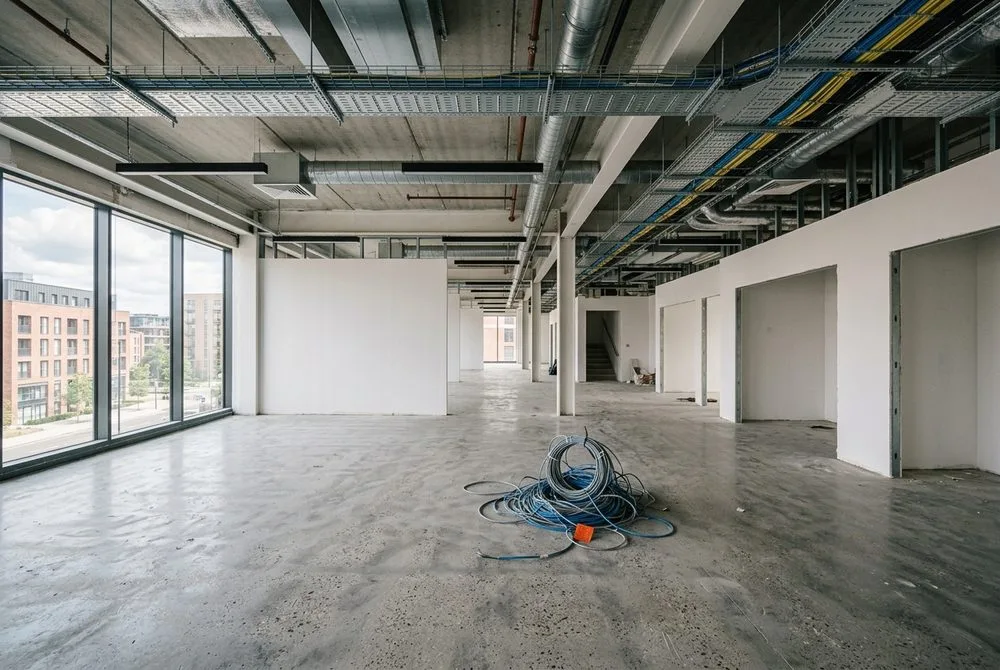 Empty commercial office space being fitted out, with cable trays overhead and network cabling on the floor, before a business move.