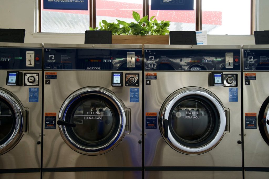 Commercial washers below the front windows with potted plants on top at The Laundry Hub SF
